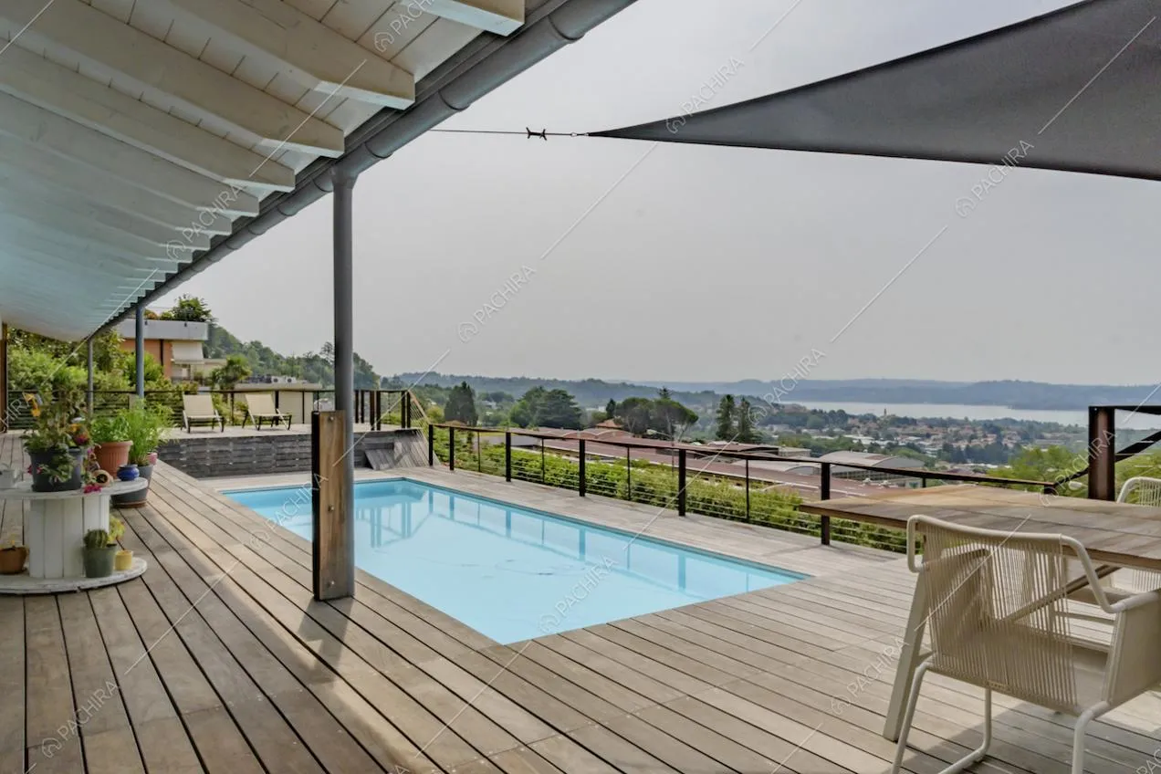 Piscina, lettini e tavolo da pranzo sulla terrazza con pavimento in parquet e vista sul lago