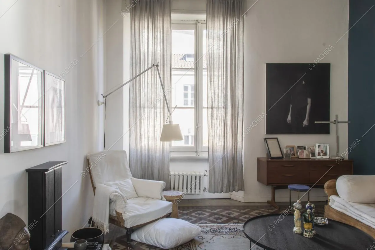 Lampada da terra vicino alla poltrona bianca e alla finestra con tende leggere