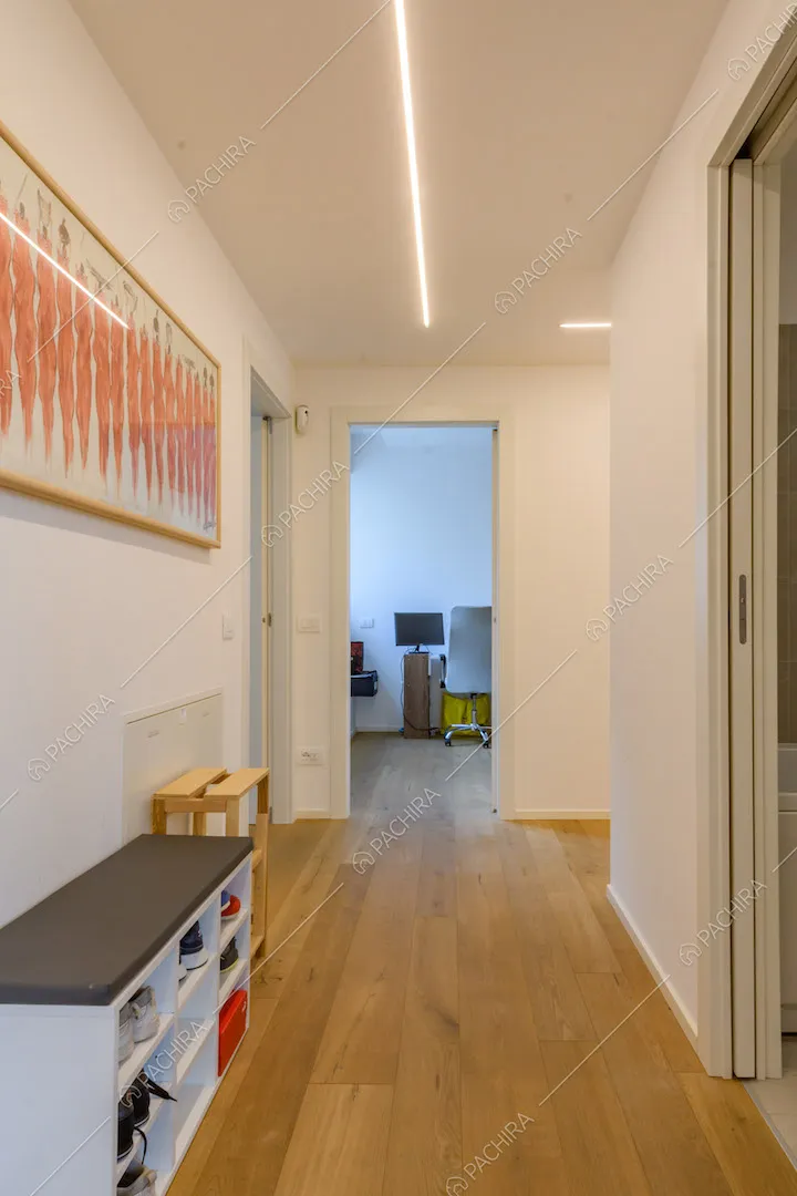 Lungo corridoio con pavimento in parquet e pareti bianche