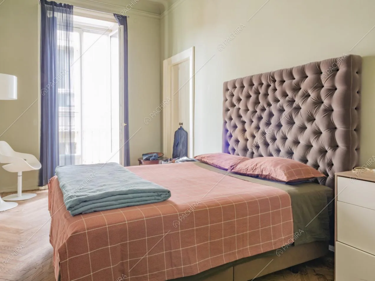 Camera da letto con tende leggere blu, sedia bianca e comodino con cassetti