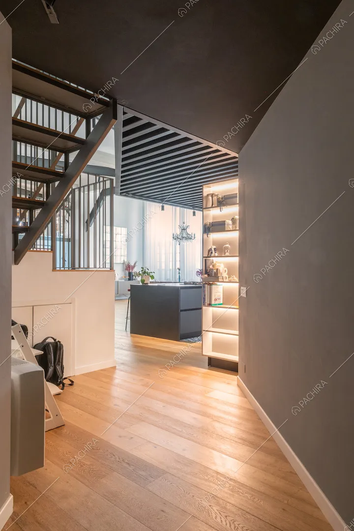 Dal corridoio con pavimento in parquet vista sull'isola nera della cucina, illuminata dalle vetrate in stile industriale