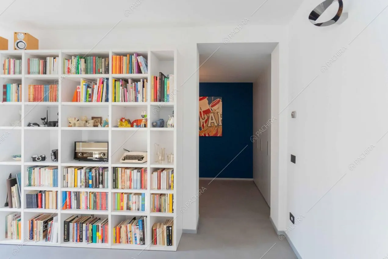 Libreria bianca nella sala e vista sulla parete blu dell'ingresso