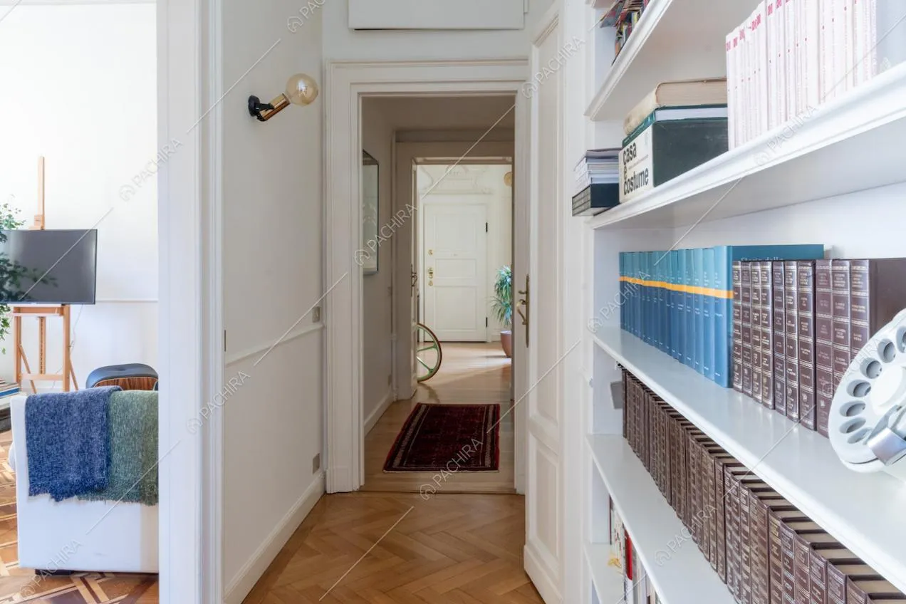 Corridoio con pavimento in parquet a spina di pesce, libreria e boiserie alle pareti