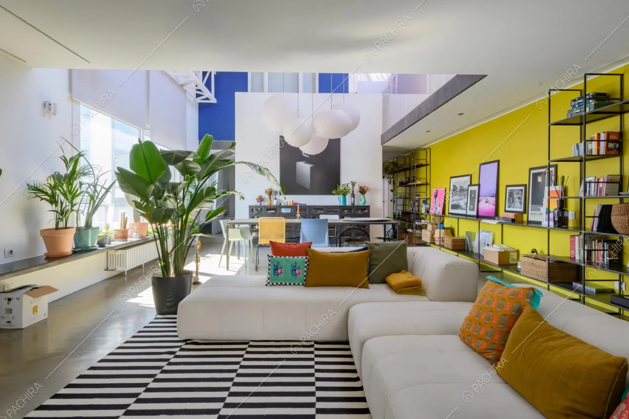 Luminosa zona living con divano bianco angolare e parete gialla con libreria