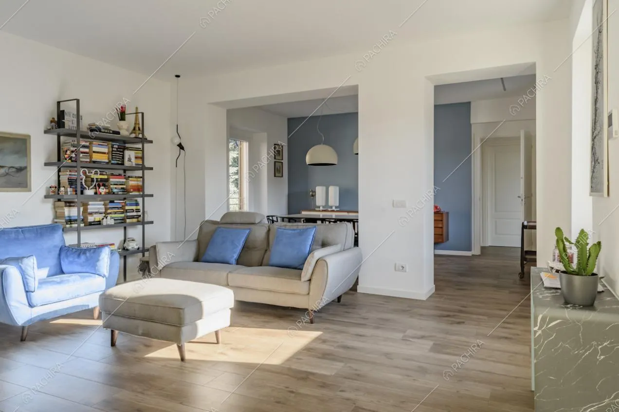 Soggiorno con divani, pouf, libreria e pavimento in parquet