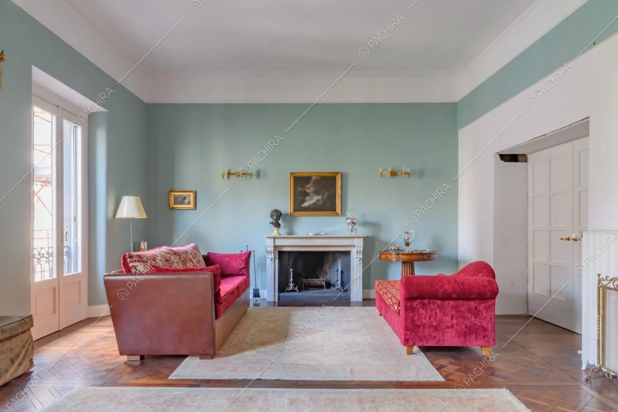 Sala dalle pareti azzurre, con porta-finestra, camino e divani in velluto rosso