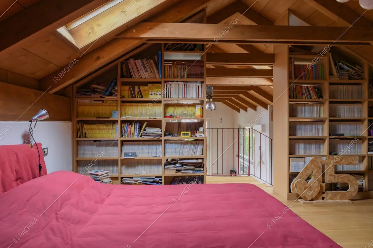 Letto matrimoniale nella camera con lucernario, soffitto in travi in legno a vista e libreria a muro