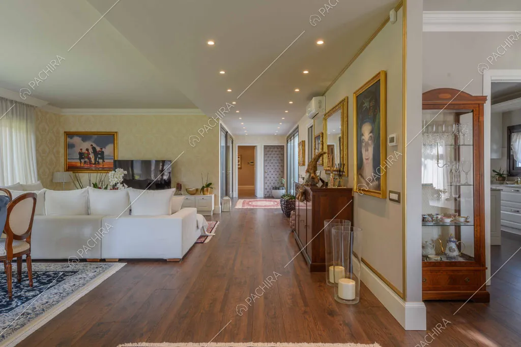 Luminosa sala con divano bianco angolare, pavimento in parquet e scorcio sulla cucina