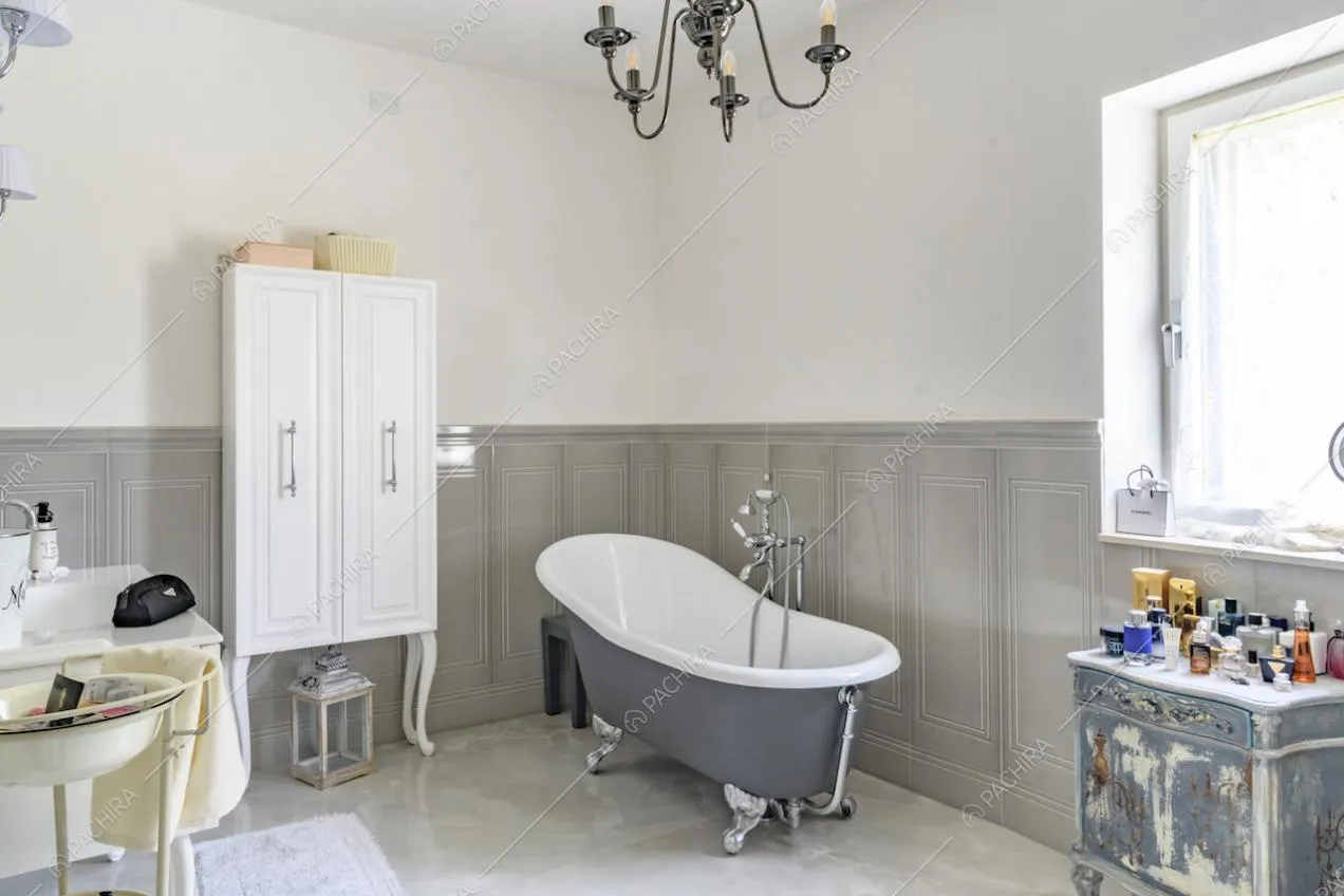 Bagno con vasca, pareti bianche e grigie con boiserie, pavimento in piastrelle e lampadario