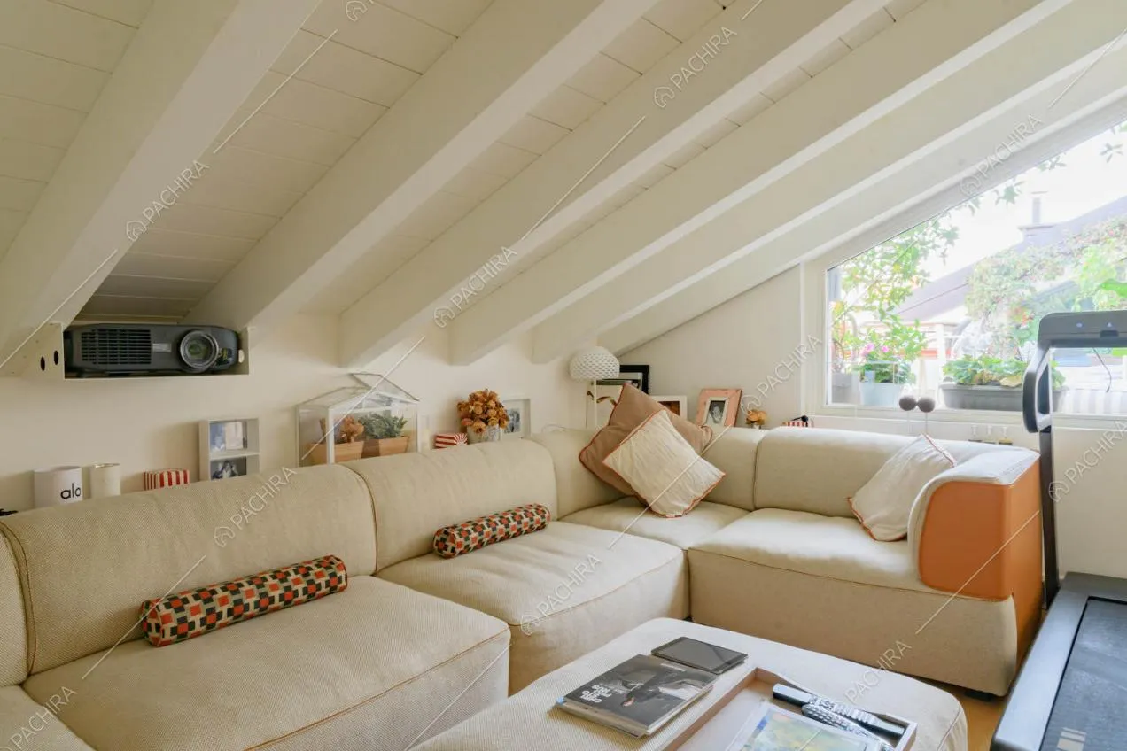 Divano angolare sul solaio con soffitto in travi bianche a vista e vetrate