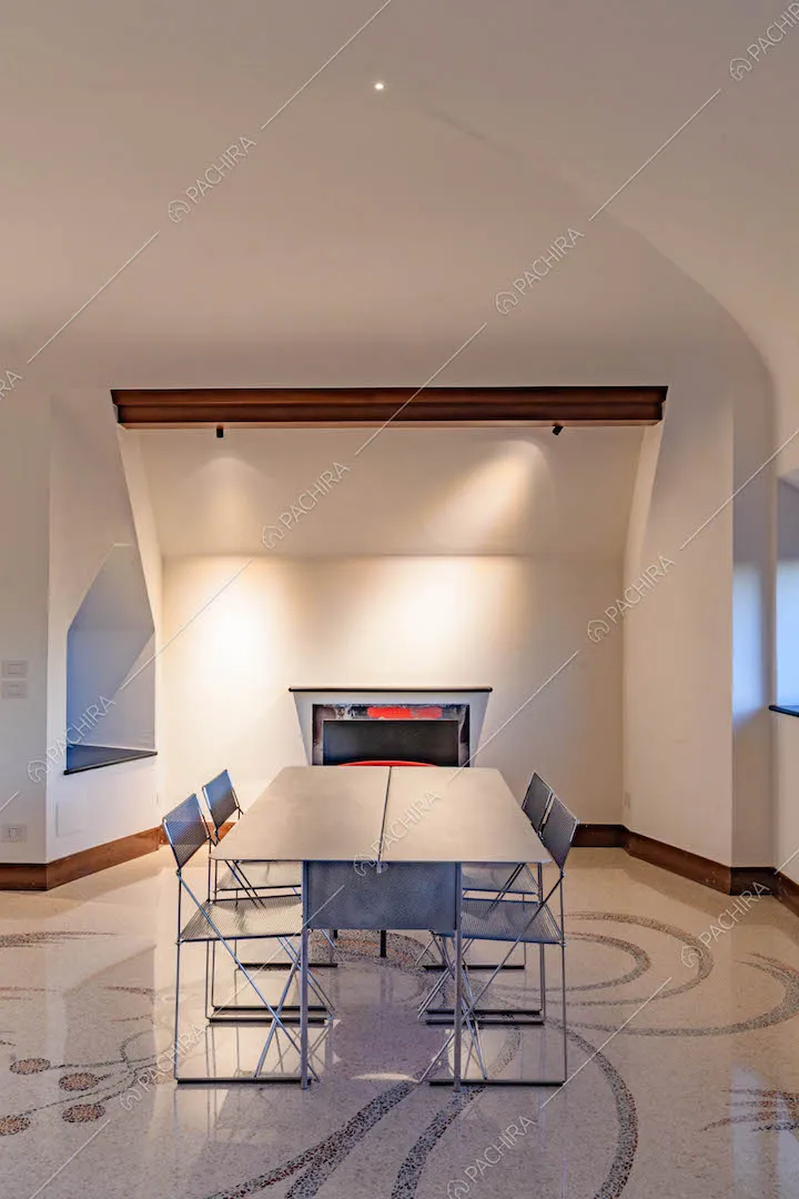 Sala con pavimento in marmo, tavolo in metallo, camino, pareti e soffitto bianchi
