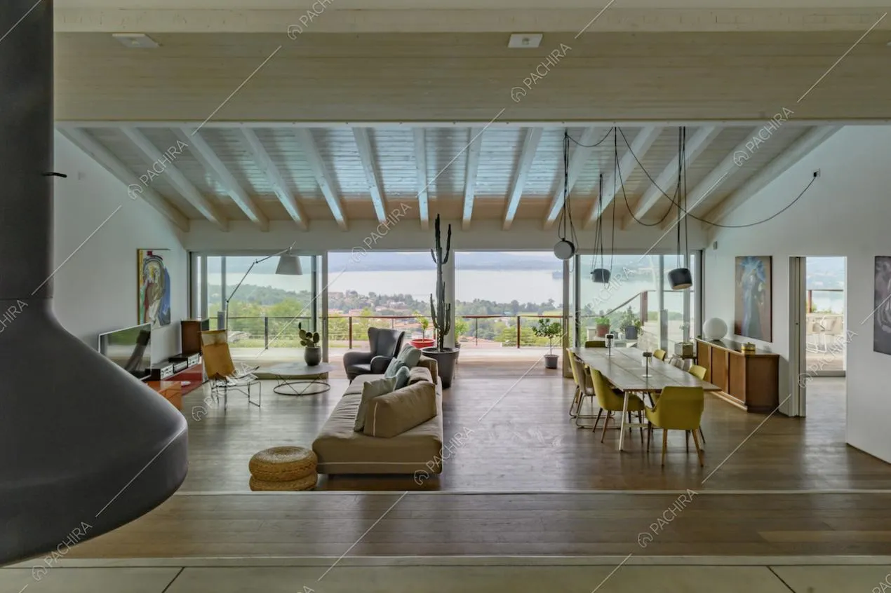 Ampio salotto con pavimento in parquet, camino su un piano rialzato e vetrate con vista sul lago