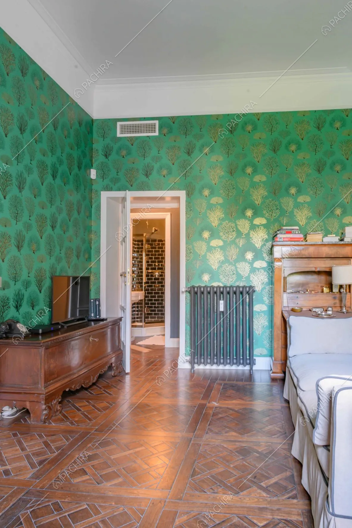 Salotto con pavimento in parquet, carta da parati verde e scorcio sul bagno con doccia