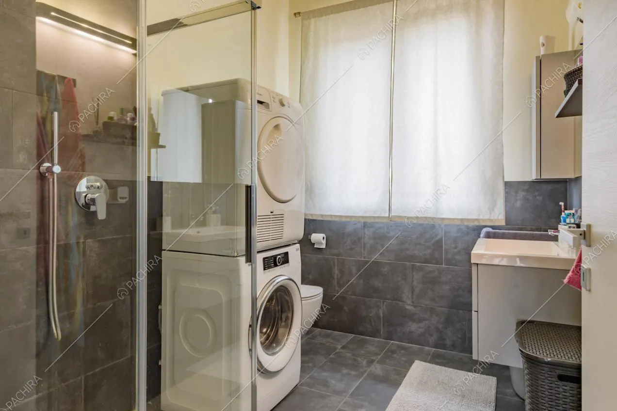 Luminoso bagno con piastrelle grigie su pavimento e pareti e box doccia