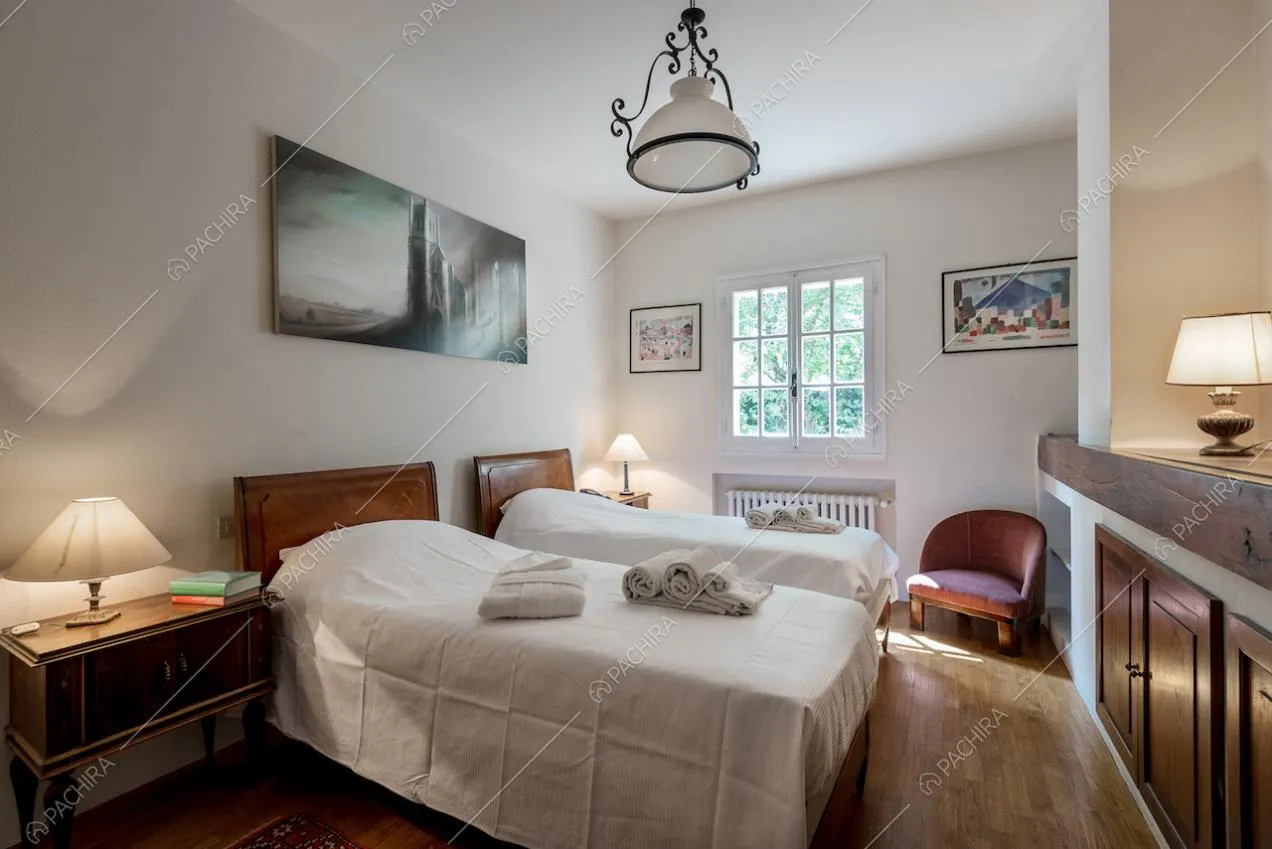 Camera da letto doppia, con pareti bianche, pavimento in parquet e poltrona rossa