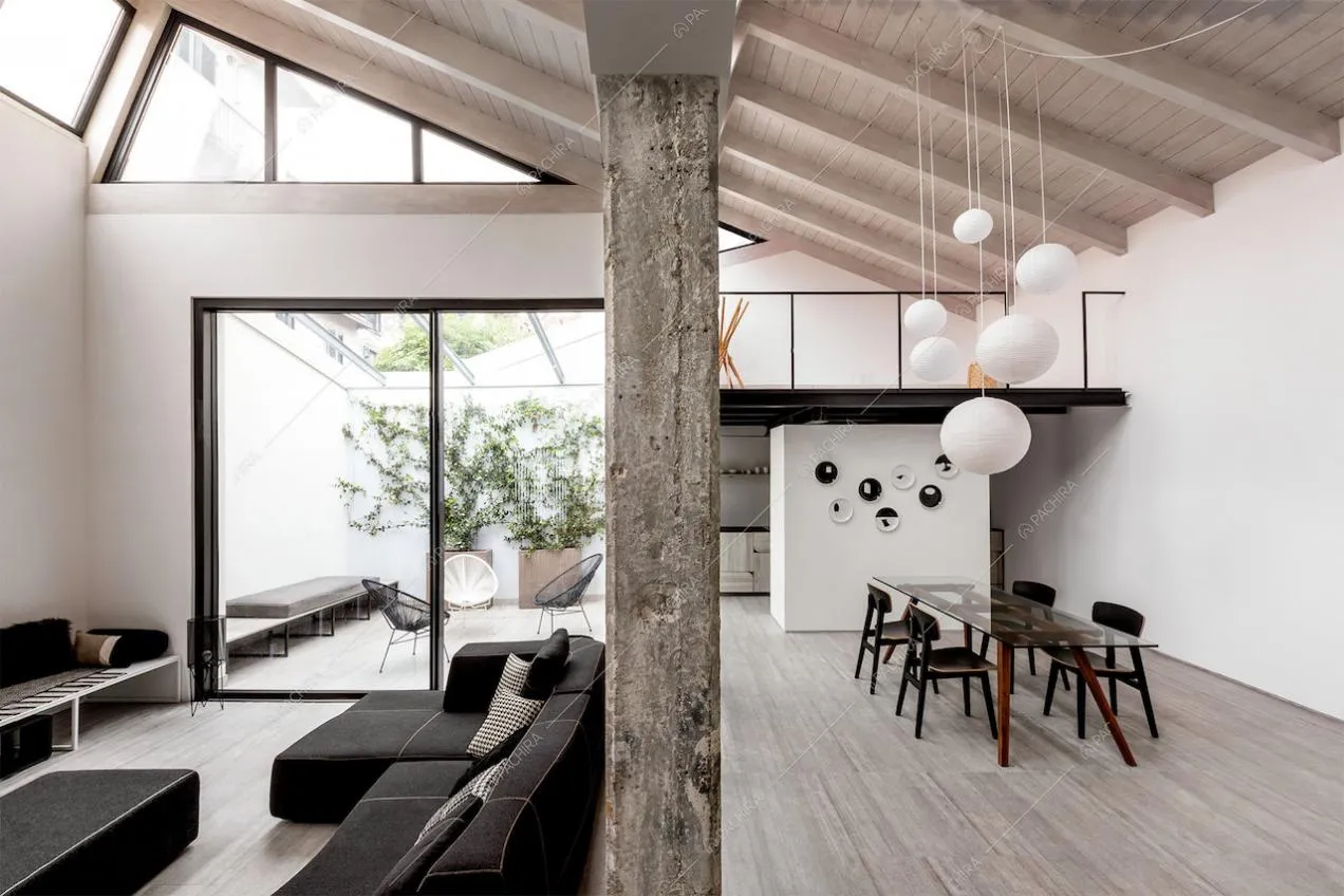 Sala con divano nero, giardino d'inverno, tavolo da pranzo e travi in legno a vista