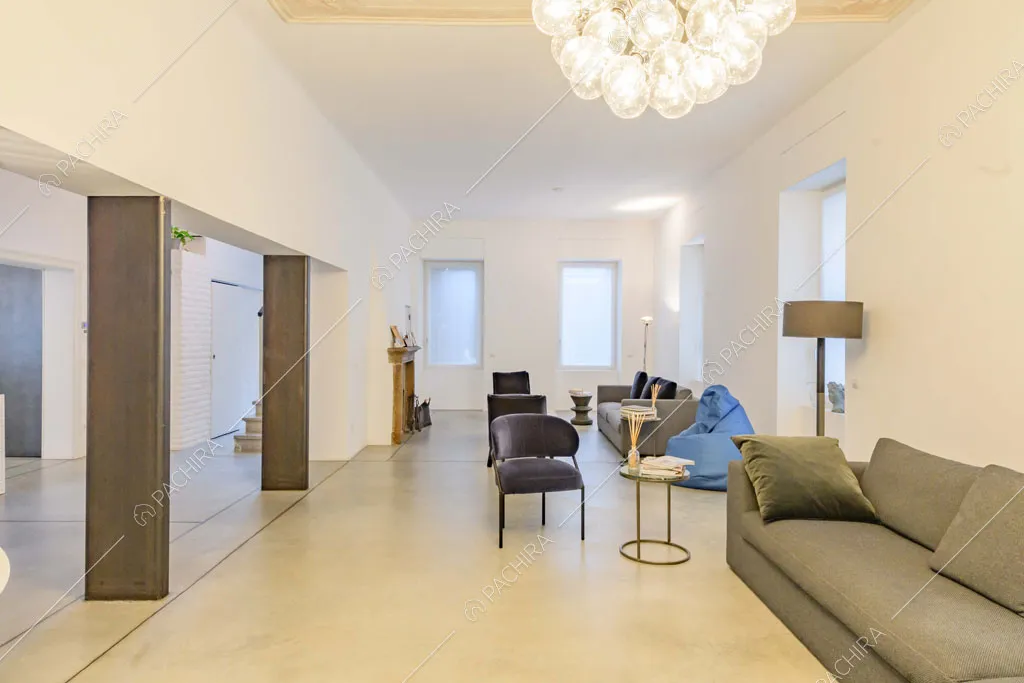 Ampia zona living con pareti e soffitto bianchi, lampadario di design e colonne in metallo a vista