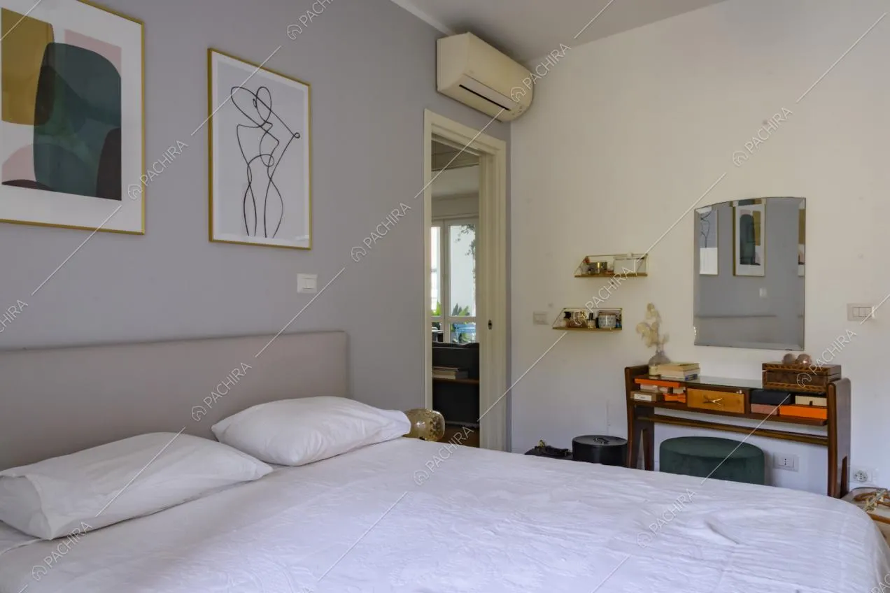 Camera matrimoniale con piccola scrivania in legno e quadri sopra alla testata del letto