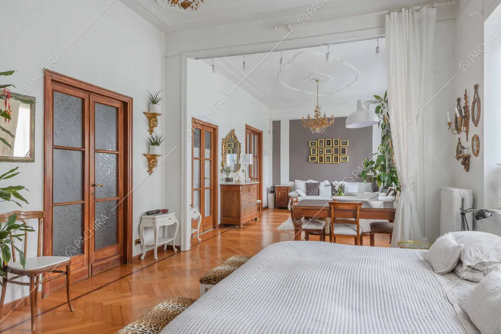 Letto matrimoniale nella grande camera con boiserie sul soffitto e pareti bianche