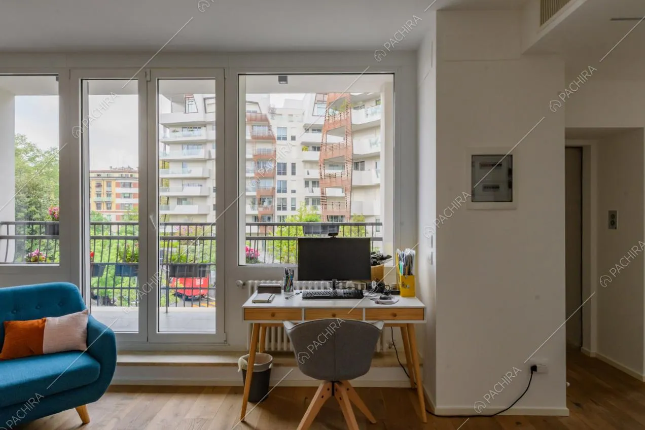 Scrivania nel salotto con divanetto blu, pavimento in parquet e porta-finestra