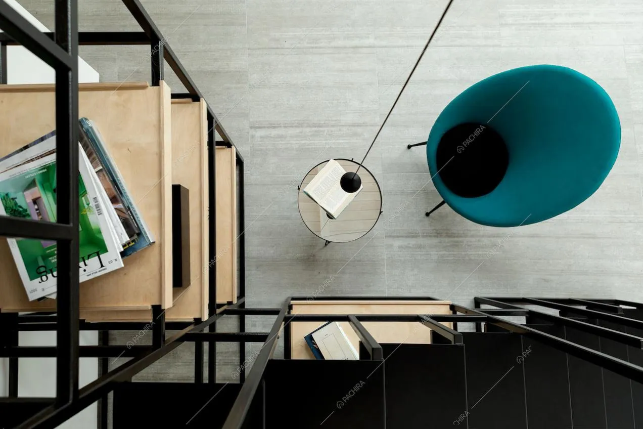 Dalle scale nere in metallo vista sui ripiani della libreria in legno e sul tavolino e poltrona di design
