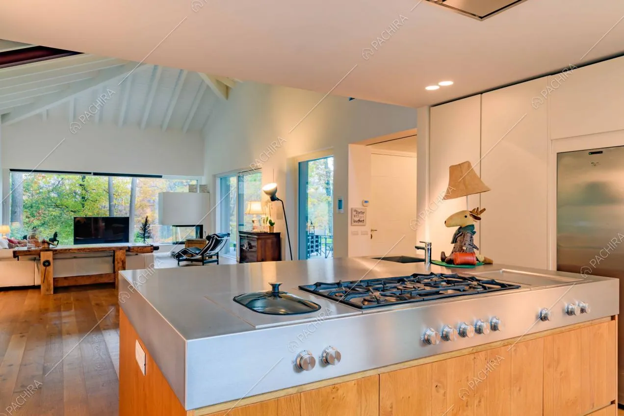 Cucina a isola con fornelli a gas, vista sul salotto e sul soffitto bianco con travi in legno