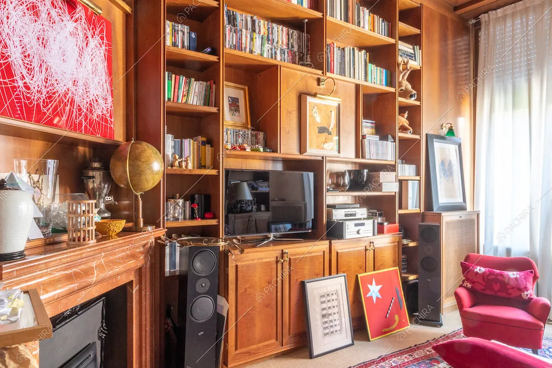 Libreria con camino e poltrone rosse nella biblioteca illuminata dalle ampie vetrate 
