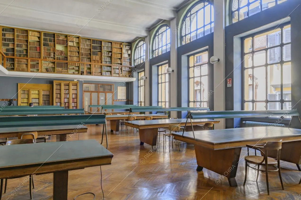 Tavoli da consultazione nella luminosa biblioteca con pavimento in parquet a spina di pesce