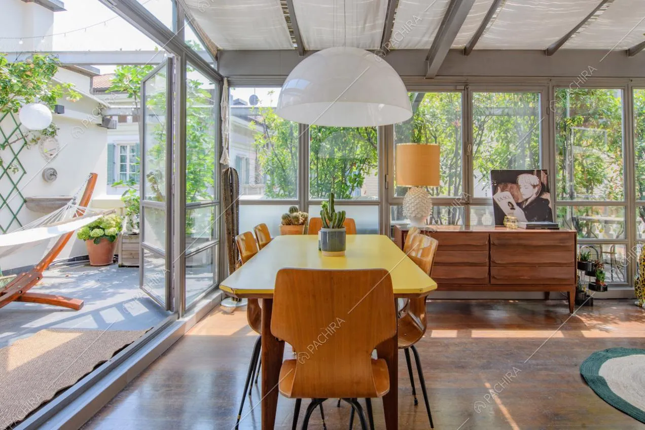 Tavolo da pranzo, sedie e lampadario di design nella veranda con pavimento in parquet