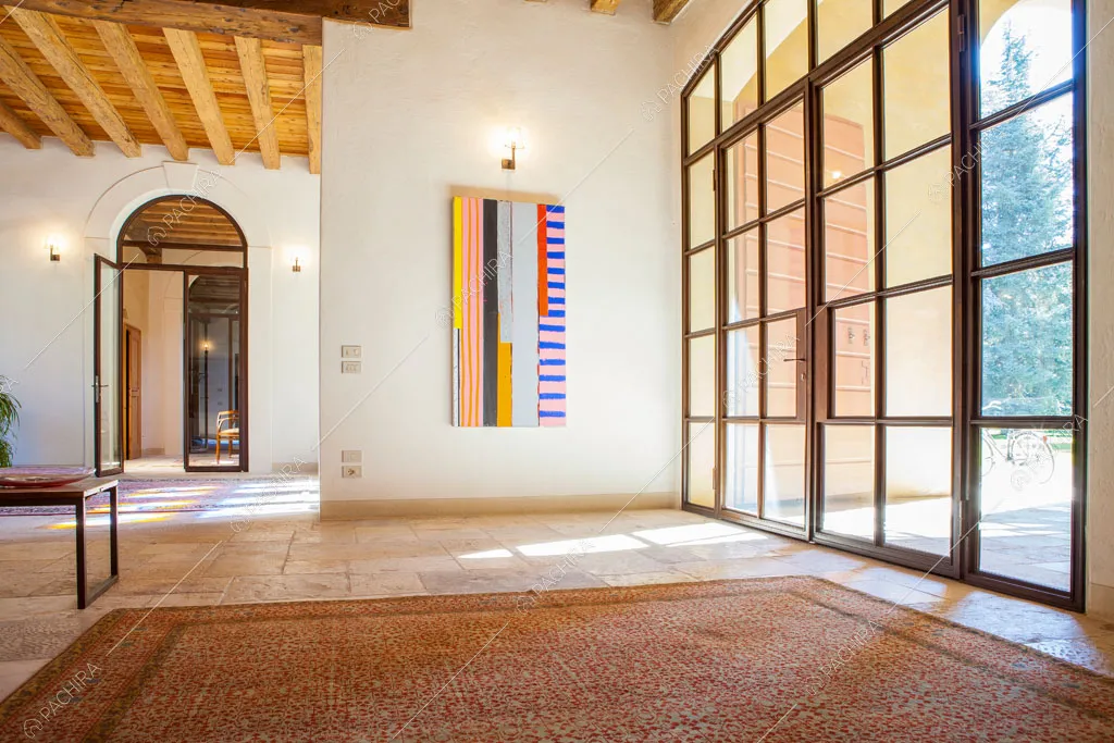 Grande sala con porta-finestra in stile industriale, pareti bianchi e travi a vista sul soffitto