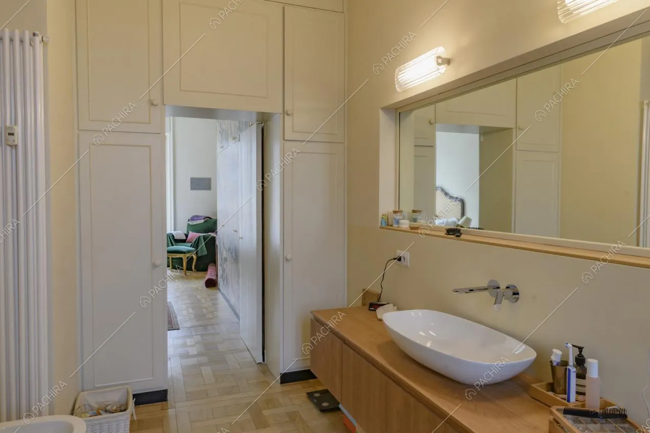 Bagno con pavimento in parquet, armadio bianco a muro e vista sulla camera da letto