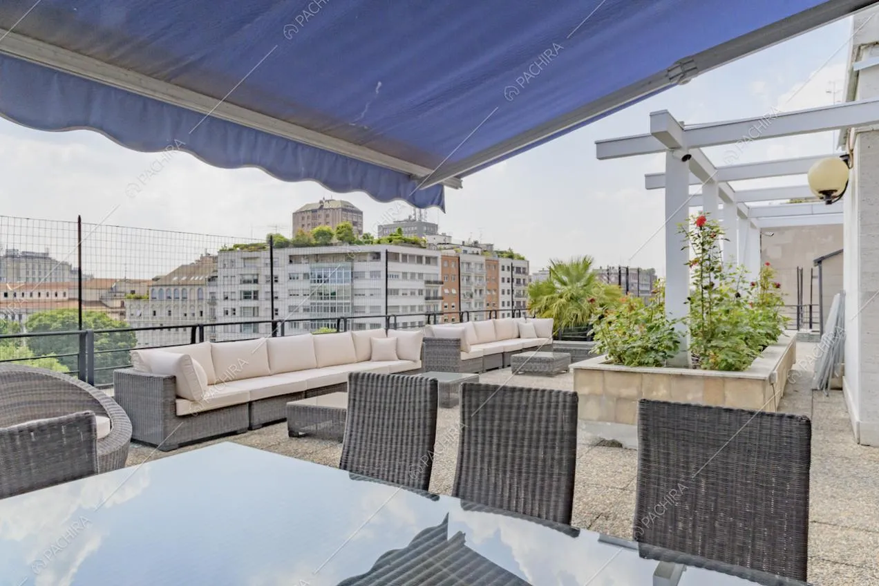 Tavolo da pranzo, riparato da un tendone blu, sulla terrazza con divani bianchi