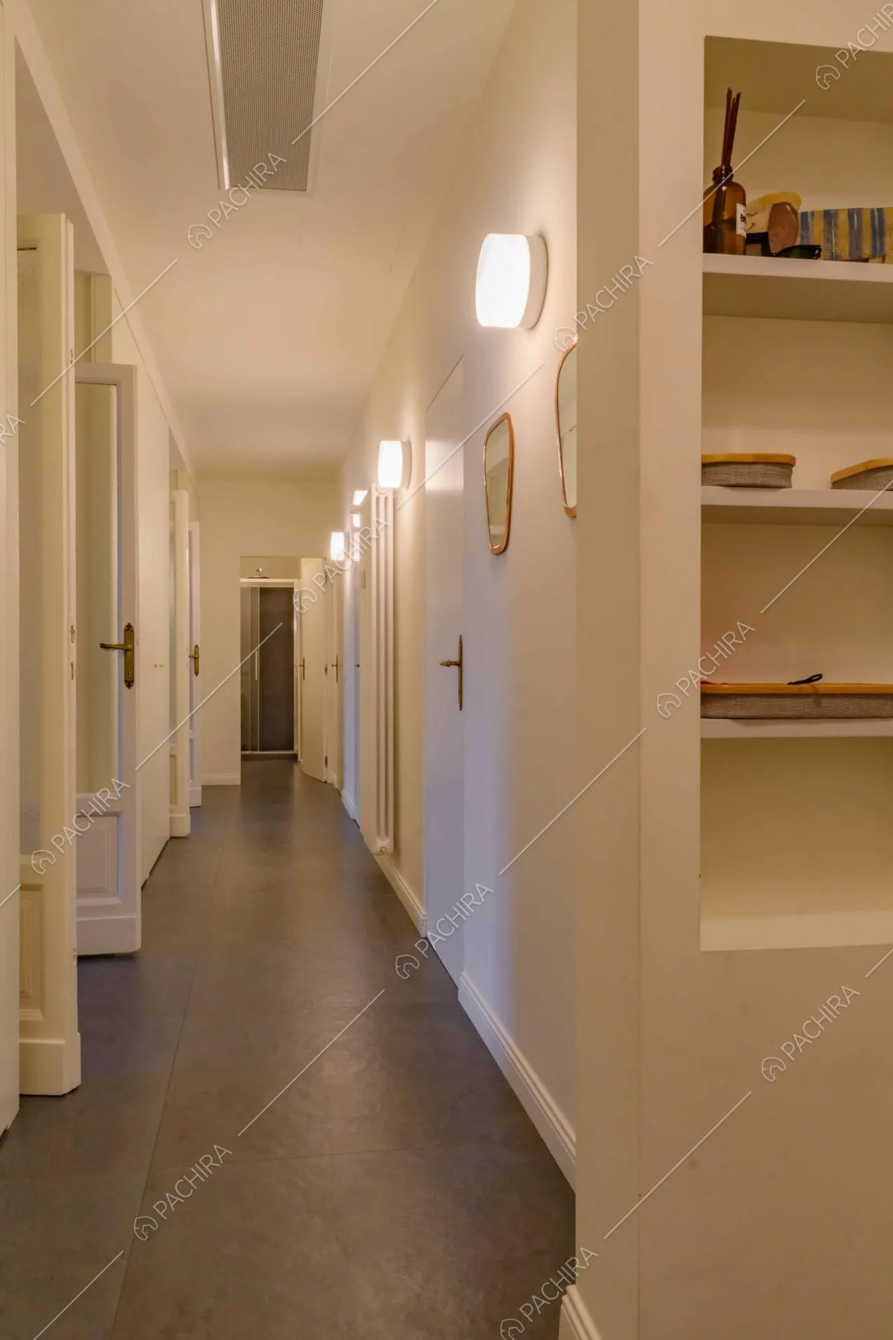 Corridoio dalle pareti bianche e dal pavimento in cemento lisciato grigio con vista sul bagno
