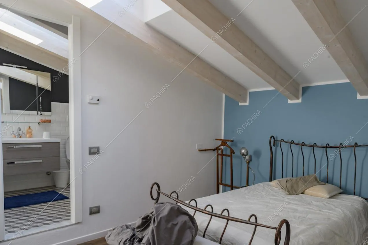 Letto matrimoniale con struttura in ferro, travi a vista e parete colorata