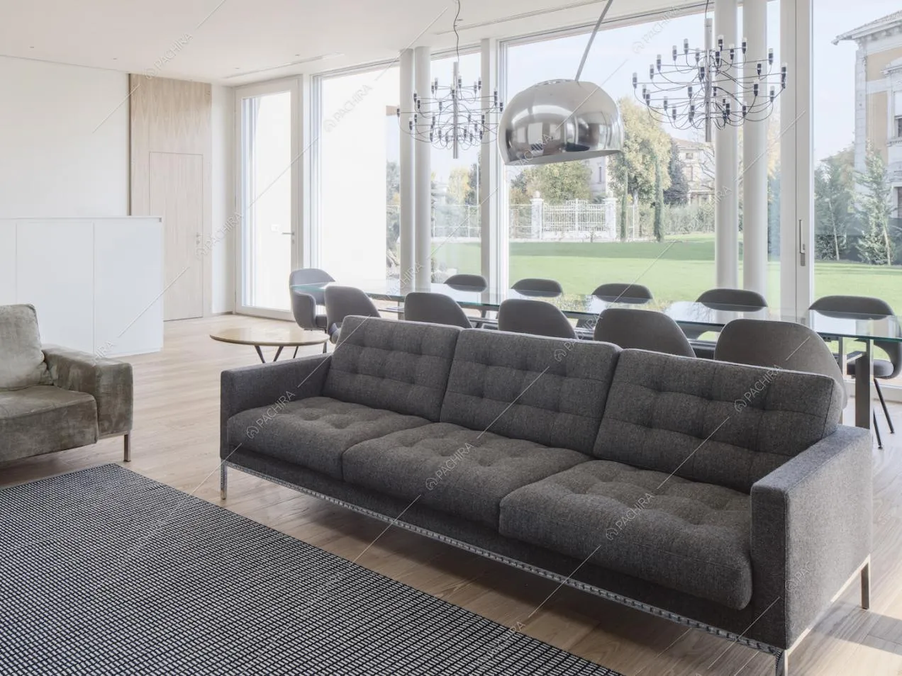 Divano grigio nella sala con lampadari di design, pavimento in parquet e porte-finestre per accedere al giardino privato