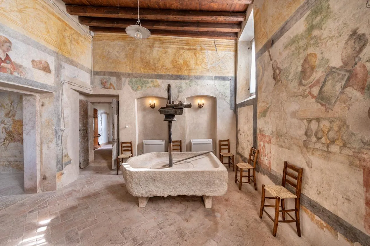 Cucina affrescata con torchio per l'uva e soffitto con travi in legno a vista