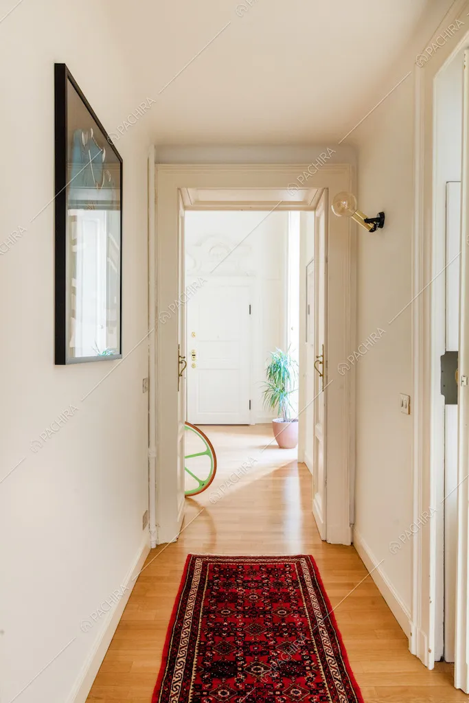 Dal corridoio con le pareti bianche e pavimento in parquet vista sulla porta d'ingresso