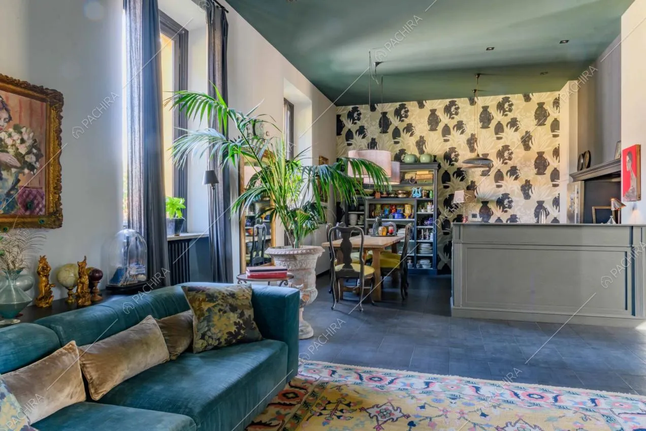Sala con divano in velluto azzurro, carta da parati e cucina a vista