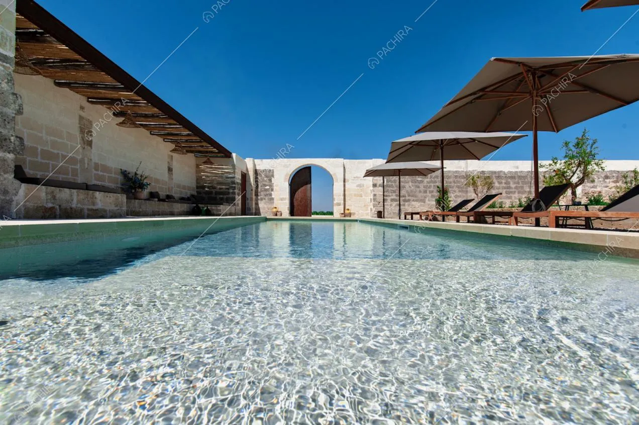 Tettoia con travi a vista, ombrelloni e portone d'ingresso intorno alla piscina