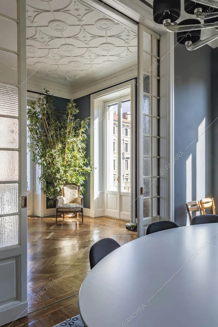Porta a vetri bianca separa il salotto con boiserie sul soffitto dalla sala da pranzo