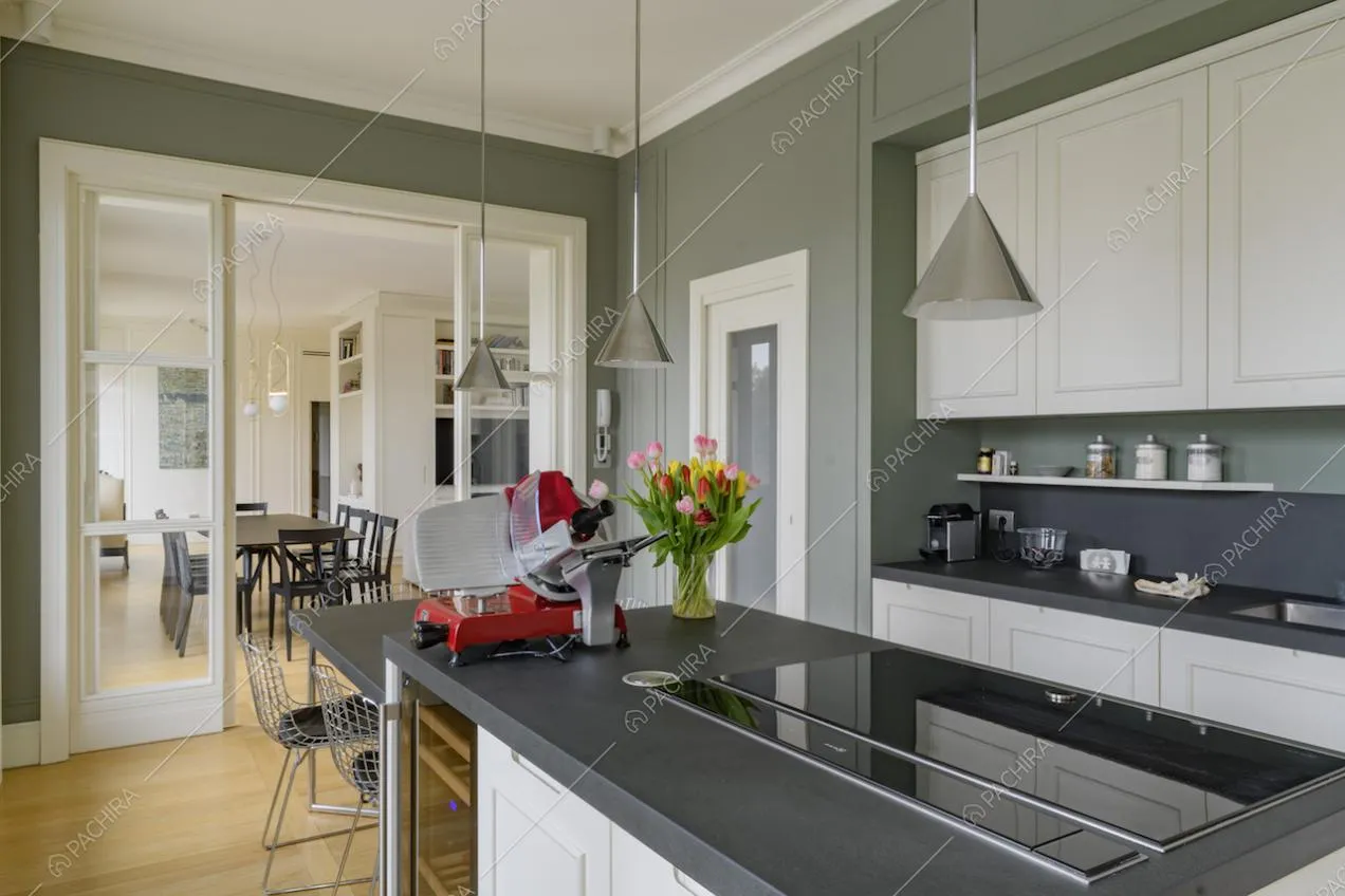 Cucina a isola con fornelli a induzione, pavimento in parquet e porte a vetri che separano sala e cucina