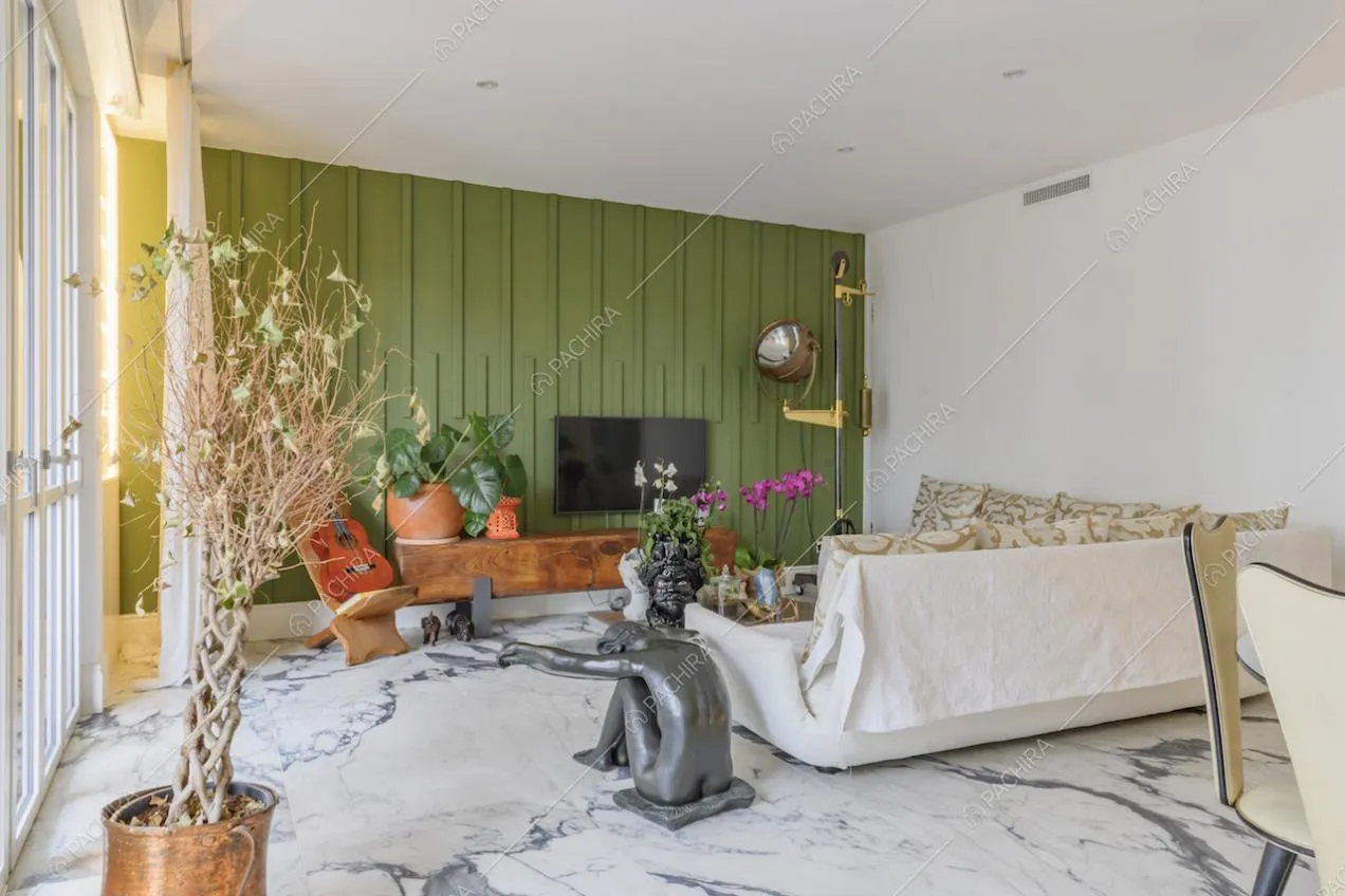 Luminoso salotto con parete verde con boiserie, divano bianco e tavolino con una statua come sostegno