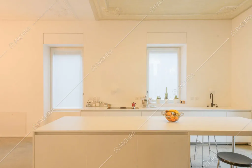 Isola bianca con sgabelli nella luminosa cucina total white con boiserie sul soffitto