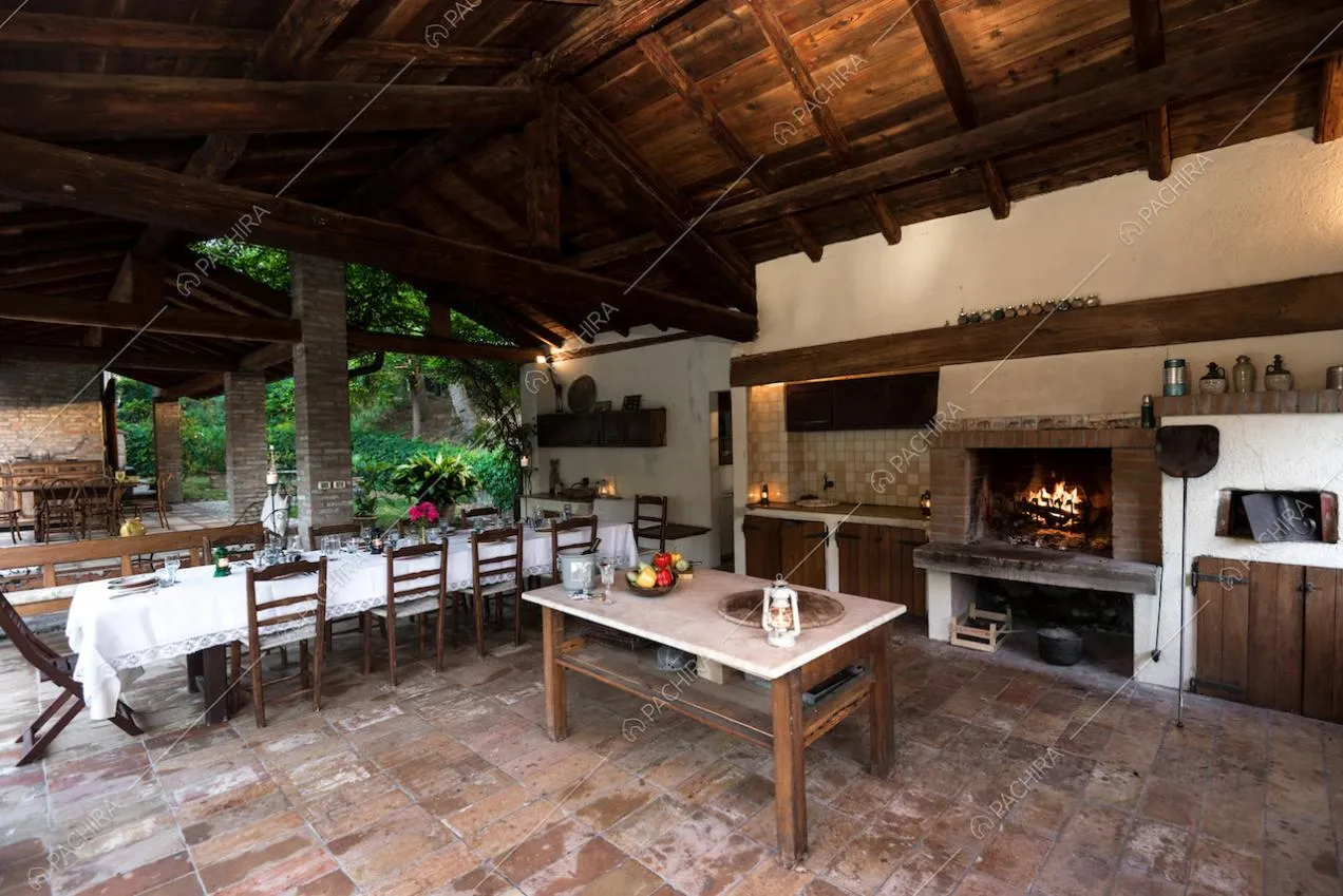 Veranda con pavimento in cotto, tavolo da pranzo, camino e soffitto in travi in lengo a vista